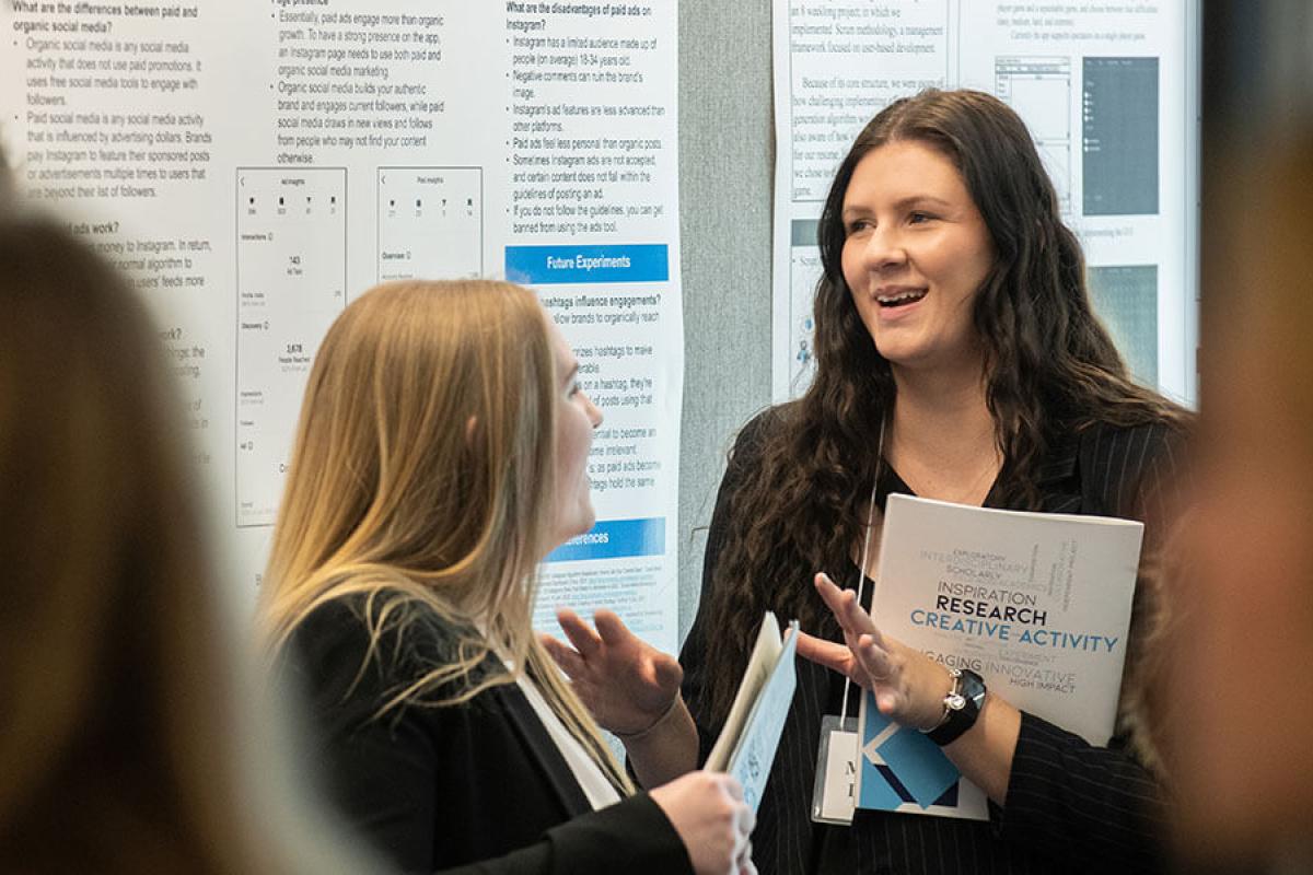 Two people engage in a discussion in front of informational posters. 