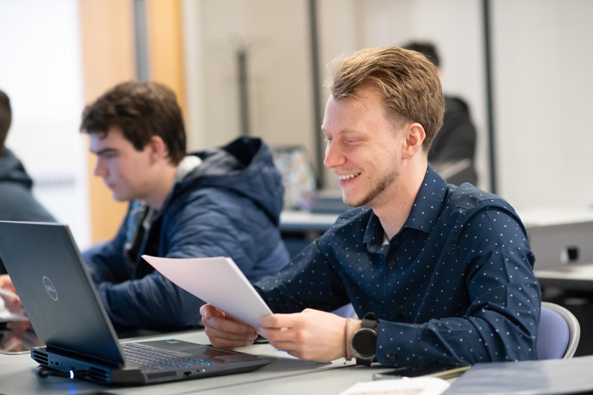 Computer science student smiling in front of lap top wearing long sleeve navy shirt.