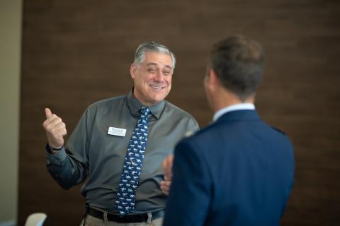 Robert Vigneault, Assistant Director of Veteran Services, wears a green, button-down shirt and blue-speckled tie. He's smiling and discussing with people at the 2023 Veteran's Day Ceremony.