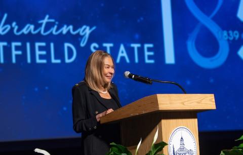 President Linda Thompson of Westfield State giving a keynote speech in front of a blue screen that says "Celebrating 185 Years of Westfield State".