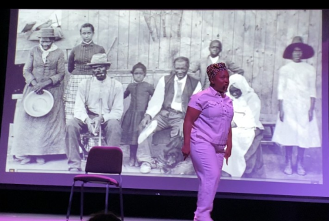 Woman performs on stage in front of black and white image of African Americans in the 19th century
