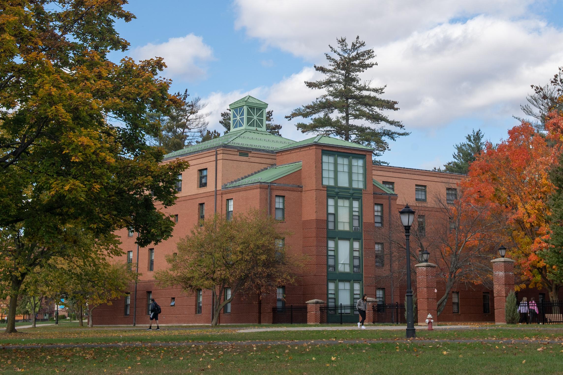 Photo of Courtney Hall with colorful autumn foliage in the courtyard and campus green.