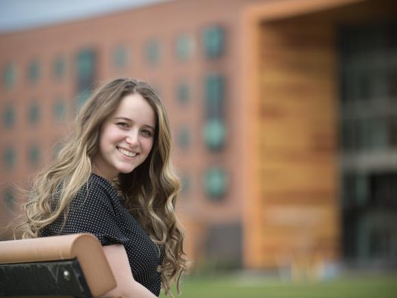 Smiling female student sitting on a bench on the campus green with University Hall in the background