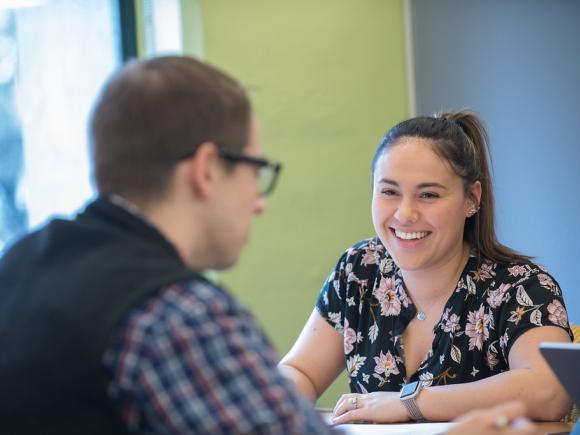 Smiling female student talks to friend across the table from her