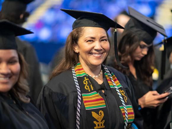 A student wearing their graduation cap and gown smiles at the camera. 