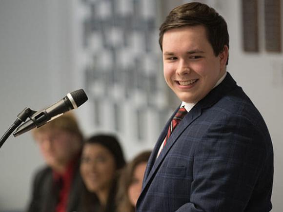 A student smiles while standing at a microphone.