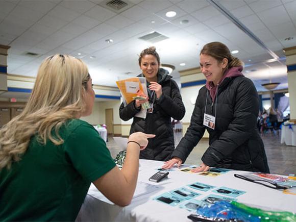 Two students conversing with someone seated at a table.