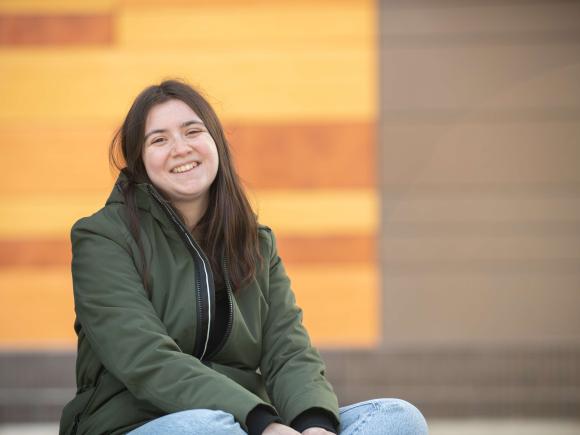 Westfield State student Cristina Ferraro sits in front of University Hall, a building with a wooden and metal facadeches and desserts in a restaurant decorated with an Alice in Wonderland theme.