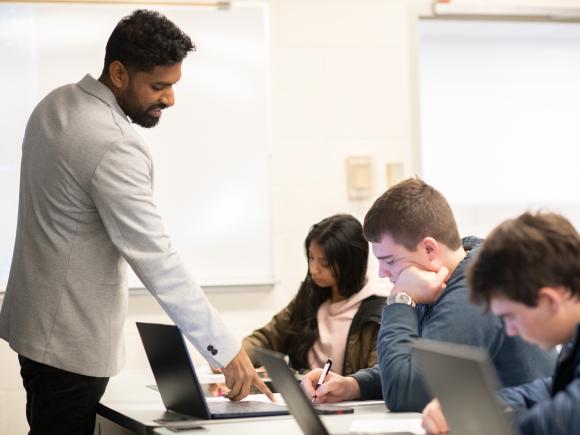 Data science faculty member in classroom with three students in front of desktop computers.