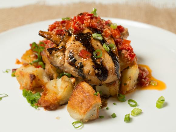 Dining services grilled chicken with red sauce on top with garnish on white plate.