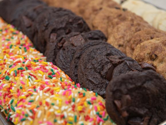 A close-up shot of three different kinds of cookies being offered in the Dining Commons. One is a white cookie with rainbow sprinkles, one is double-chocolate, and the third are brown cookies with chocolate chips.