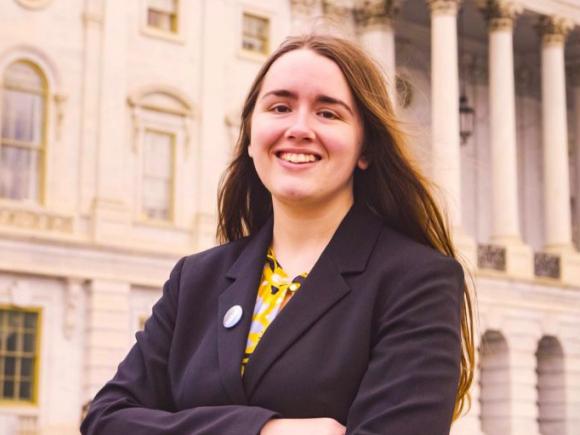 Erin Crosby wears a black, long-sleeved jacket and has her arms folded across her chest. She stands in front of a white government building, as she was featured by the US Department of Education for her work in disability services.