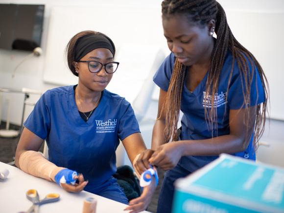 Splinting lab featuring two health science students in blue scrubs with WSU logos testing how to splint on eachother. 