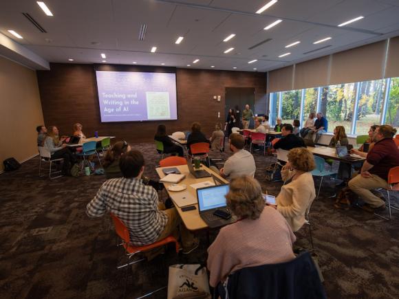 Attendees of the WMWP's AI Workshop event. They sit at tables and face towards the front of the room where a screen reads: "Teaching and Writing in the Age of AI."