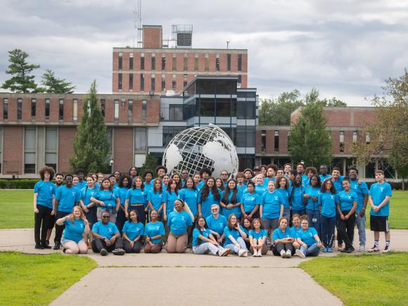 Urban Education group photo in front of campus globe with students wearing blue tee shirts.