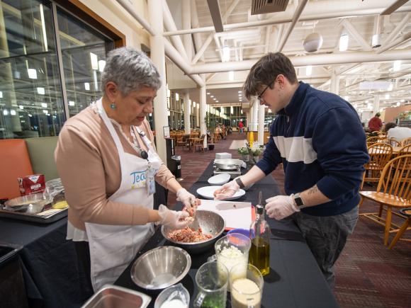 Cooking class with Maria in the Dining Commons. Photo of Maria and participant making Greek meatballs.