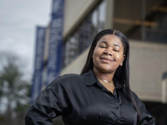 Ketia Valme, an English major and class of 2024, wears a black, long-sleeved shirt and smiles before the Ely center. 