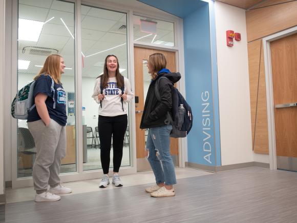 Parenzo Hall Advising Office with three students standing outside wearing WSU shirts and backpacks.