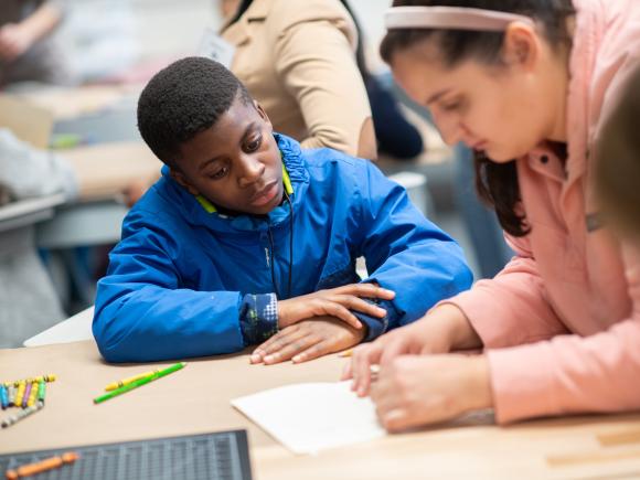 Westfield State education major and elementary school aged child sit at a desk and work together on a paper project