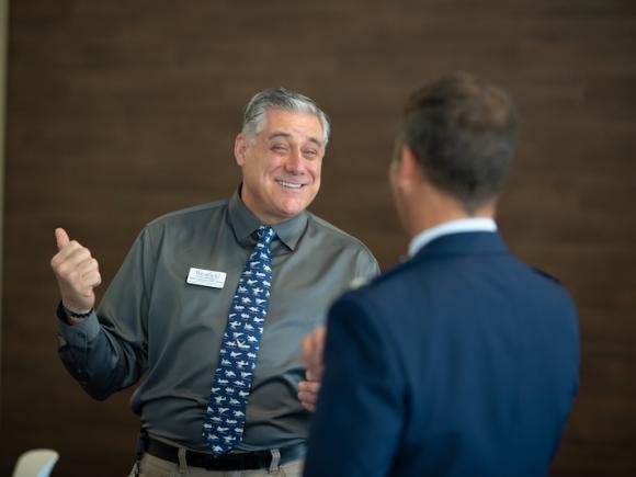 Robert Vigneault, Assistant Director of Veteran Services, wears a green, button-down shirt and blue-speckled tie. He's smiling and discussing with people at the 2023 Veteran's Day Ceremony.