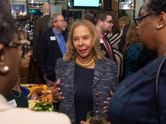 President Linda Thompson of Westfield State talking to attendees of last week's Keeper of the Dream dinner. She is wearing a yellow pearl necklace, blue undershot, and dark blue blazer.