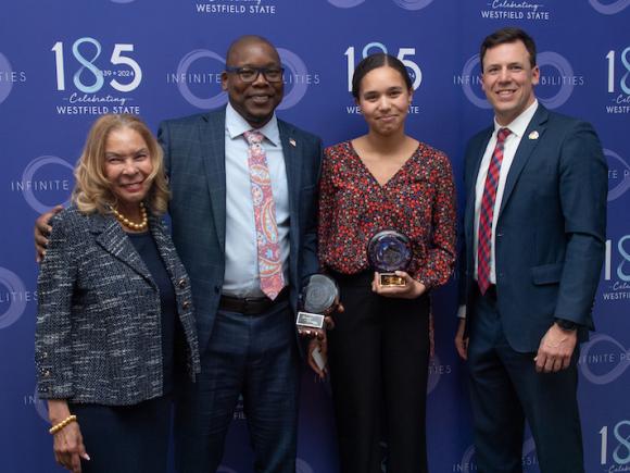 President Thompson, Mustafa & Addison Thompson, and West Springfield mayor William Reichelt at the Keeper of the Dream dinner. They stand in front of a dark blue backdrop and Mustafa and Addison have awards in their hands as two of the night's honorees.