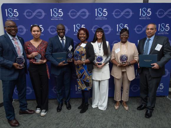 Honorees of this year's Keeper of the Dream dinner. Mustafa Thompson, Addison Thompson, Ronald Gibbons, Petrina Fondakowski, Tania M. Barber, LaToya Wilson and Tyrone Abrahamian stand side by side in front of a blue backdrop with "185th" printed all over it.