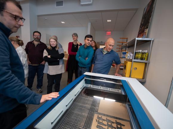 Faculty and staff surround a 3D printer in the RIDE Center at Parenzo Hall. There are various members all watching as demonstrations show how to use the technology there.