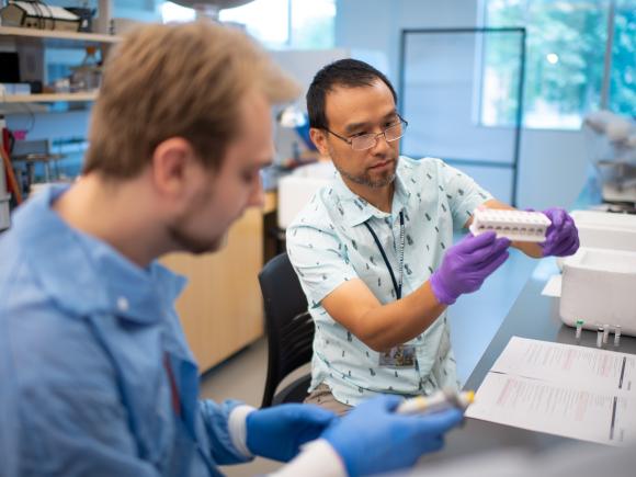 Student wearing blue lab protection gear working with advisor Dr. Mao-Lun Weng in one of the labs in the Nettie Stevens Science Center. 