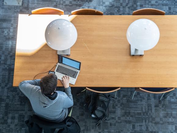 Campus library table with two lamps and student working on a laptop.