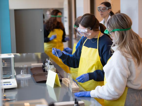 Students in chemistry classroom wearing lab aprons and eye protection.