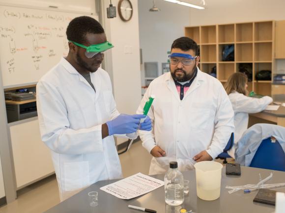 Chemistry student and professor in white lab coats working together in classroom.