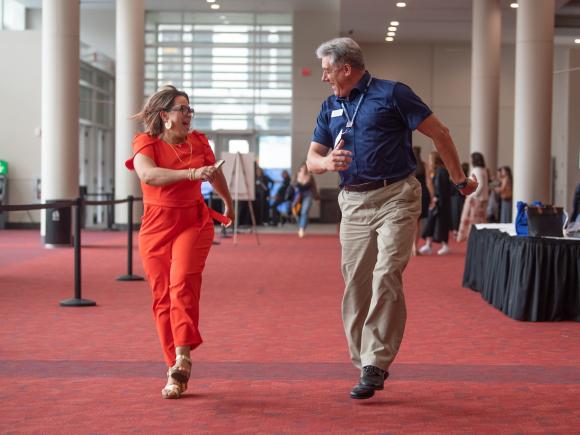 Two employees at commencement smiling and jumping together ecstatically.