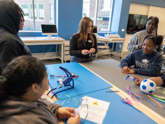 Grace Templeton of the RIDE Center during the Junior Discover program, an initiative that allows schools in the Springfield and Holyoke school systems to experience campus life. They are working on a project at the RIDE Center, and several students sit around her at their desk.