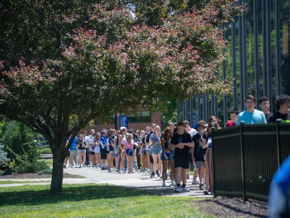 A photo of students lining up for New Orientation Day. They gather outside of the Dining Commons in rough rows of two.