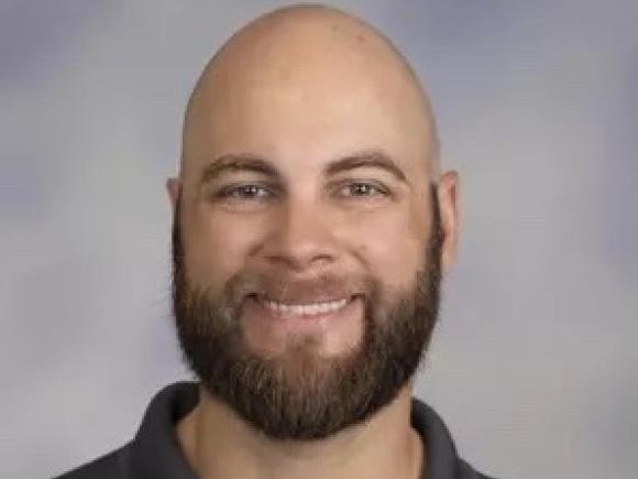 Alum Jake Suval. He is wearing a gray polo shirt and is posed in front of a professional, gray background.