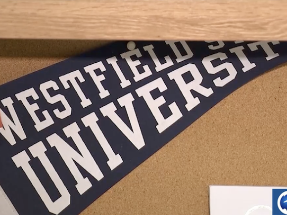 A close-up photo of a blue Westfield State University flag tacked to a cork board in a student dorm room.