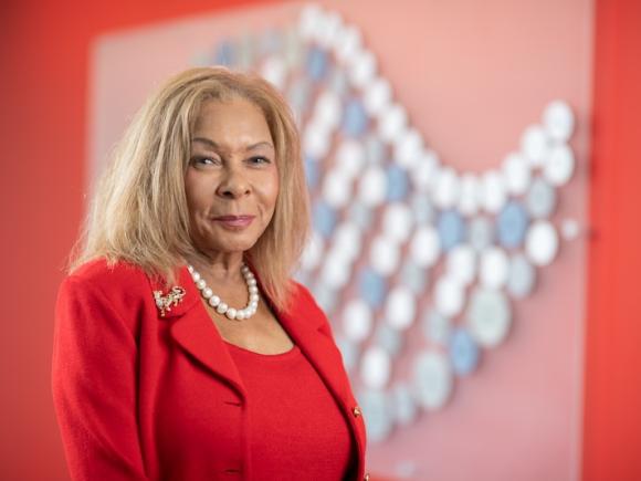 President Linda Thompson of Westfield State. She's wearing a red suit and is posed before a red mosaic wall in the Nettie Stevens Science and Innovcation building