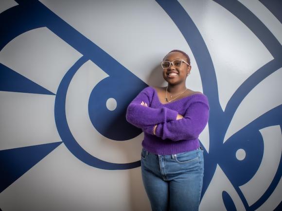 Catrina Casting, class of 2026. She is posing in front of a navy blue and white owl, and wears a purple shirt and jeans.