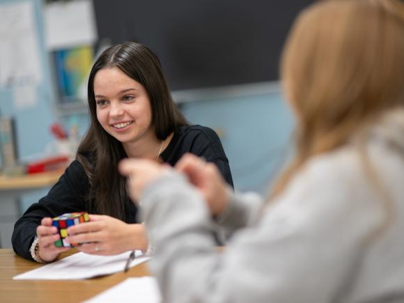 Math tutor smiling in the tutoring center with a Rubik's Cube on the desk.