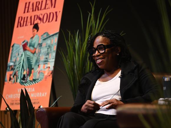 Woman smiles in front of a poster of a book cover