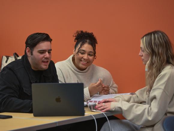Three students working on a classroom project together looking at a laptop.