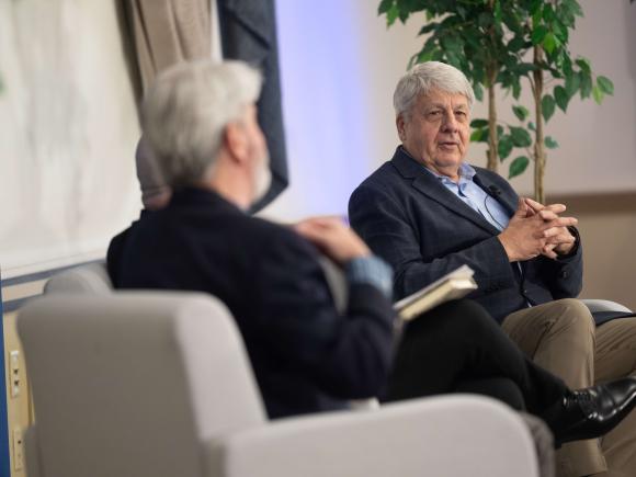 Men sit on a stage having a conversation