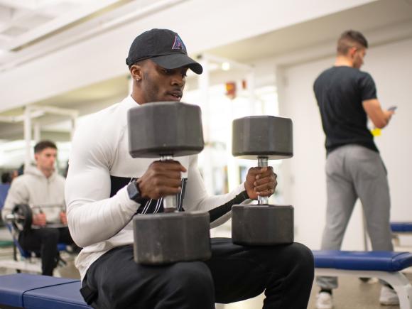 Student performing a strength training exercise with free weights.