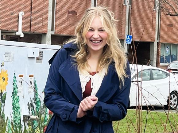 Student smiling on campus with a garden scene painting behind them.