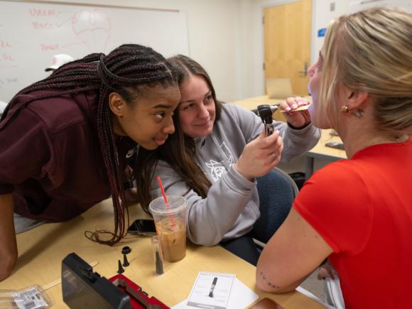 Three students learn to use an otoscope and ophthalmoscope in a classroom activity.