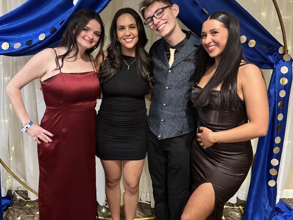 Group of students stand in front of formal backdrop
