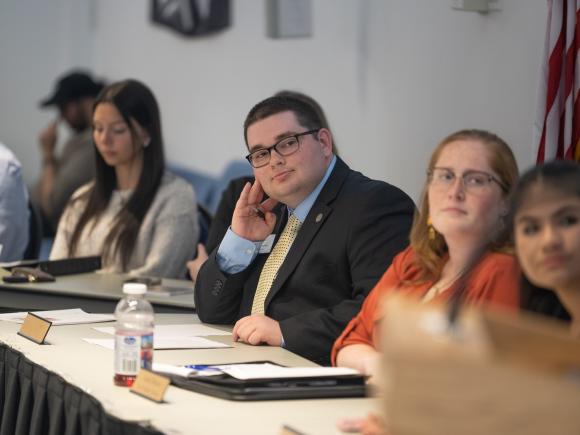 Student Government Association members seated at a table listening to a guest speaker.