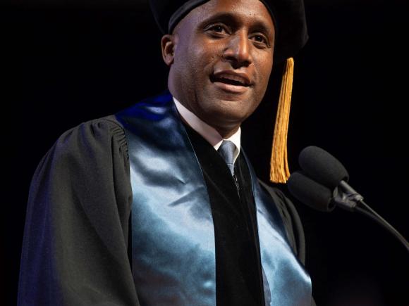 Man speaks at podium in academic regalia