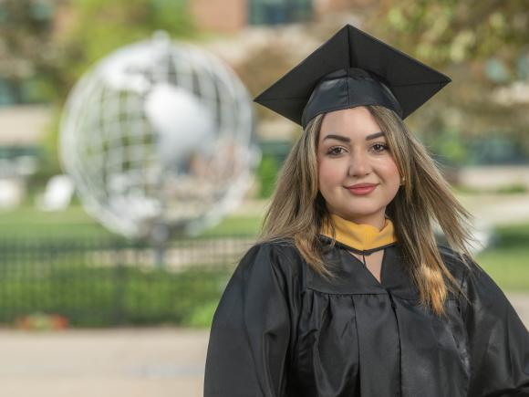 Student smiling wearing cap and gown in front of the campus globe.